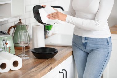 Güzel genç bir kadın bulaşık takımlarını kağıt havlularla siliyor.