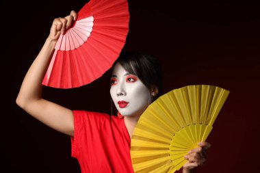 Geleneksel kıyafetler içinde, siyah arka planda hayranları olan güzel bir geyşa.