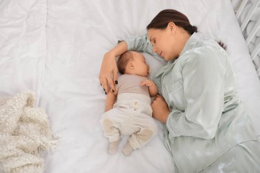 Anne, tatlı küçük bebeğiyle evde, yatağında uyuyor.
