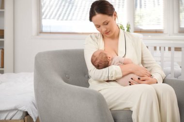 Annesi evdeki koltukta uyuyan bebeğini emziriyor.