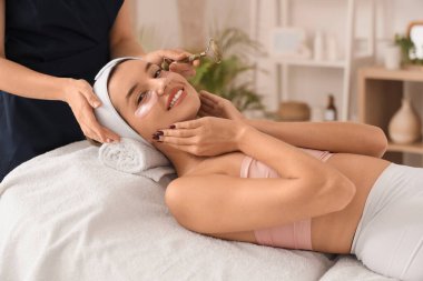 Göz altı bantlı genç bir kadın güzellik salonunda yüz masajı yaptırıyor.