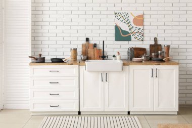 Farklı çatal bıçak, soba ve lavabo mutfak içindeki beyaz tuğla duvarın yanında.
