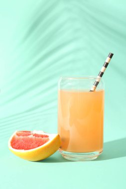 Renkli arka planda bir bardak taze greyfurt suyu ve palmiye yaprağı gölgesi