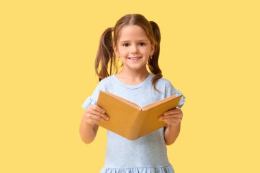 Sarı arka planda kitabı olan mutlu küçük bir kızın portresi