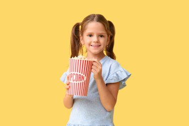 Sarı arka planda patlamış mısırı olan mutlu küçük kız.