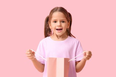 Pembe arka planda alışveriş çantası olan mutlu küçük kız.