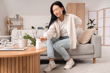 Evdeki kanepede sırt ağrısı çeken bir kavanoz hapla güzel bir Asyalı kadın.