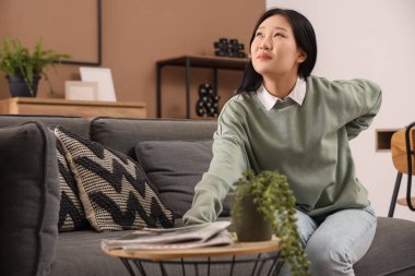 Evdeki kanepede sırt ağrısı çeken güzel bir Asyalı kadın.