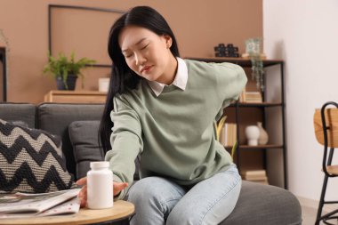 Evdeki kanepede sırt ağrısı çeken bir kavanoz hapla güzel bir Asyalı kadın.