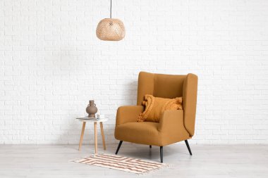 Koltuk, kahve masası, beyaz tuğla duvarın yanında dergiler ve vazo.