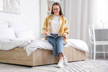 Yatak odasında dergi okuyan genç bir kadın.