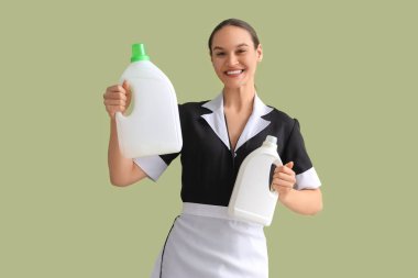 Yeşil arka planda boş çamaşır deterjanı şişeleri olan genç oda hizmetçisi.
