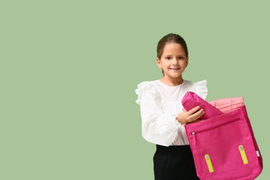 Yeşil arka planda sırt çantası ve kalem çantası olan şirin, mutlu bir kız.