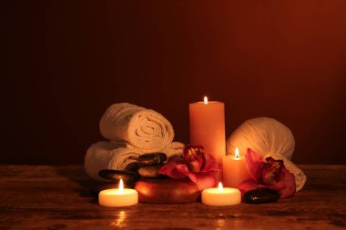 Koyu ahşap masa üzerinde yanan mumlar ve orkide çiçekleriyle güzel bir spa kompozisyonu.