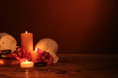 Koyu ahşap masa üzerinde yanan mumlar ve orkide çiçekleriyle güzel bir spa kompozisyonu.