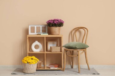 İçinde kasımpatı çiçekleri olan sepetler ve bej arka planda sandalye yakınındaki raflarda ev dekorasyonu.