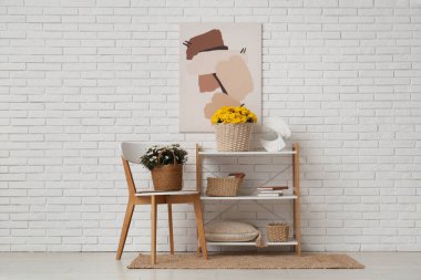 Kasımpatı çiçekli sepetler ve beyaz tuğla duvara karşı sandalyenin yanındaki raf ünitesinde ev dekoru.