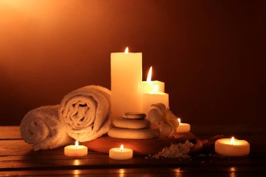 Mumları havlularla yakmak, tesisat çiçeği, deniz tuzu ve ahşap masa üzerinde koyu arkaplan ile spa taşları