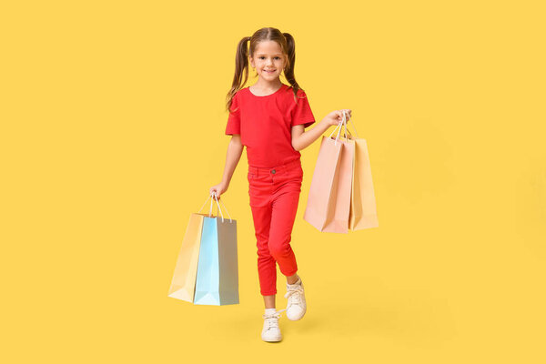 Портрет счастливой маленькой девочки с пакетами покупок на желтом фоне