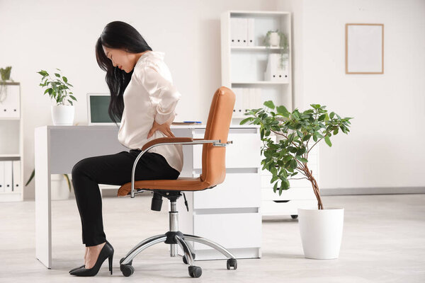 Beautiful young Asian businesswoman suffering from back pain on chair in office