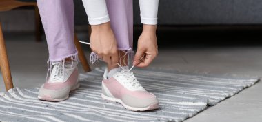 Evde ayakkabı bağcıkları bağlayan genç bir kadın, yakın plan.