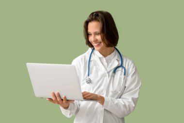 Yeşil arka planda modern dizüstü bilgisayarı olan güzel bir kadın doktor.