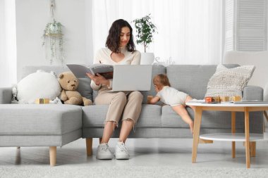 Sevimli küçük bebek ve evde doğum iznini okurken dizüstü bilgisayarla çalışan mutlu genç anne.