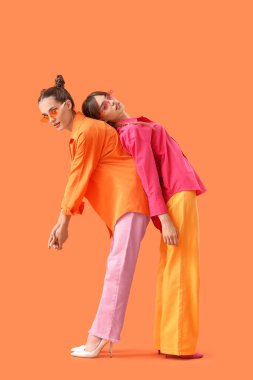 Turuncu arka planda poz veren şık elbiseli güzel, genç, moda kız kardeşler.