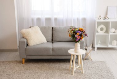 Oturma odasındaki sehpanın üzerinde yabani çiçekler olan kanepe, raf ünitesi ve vazo.