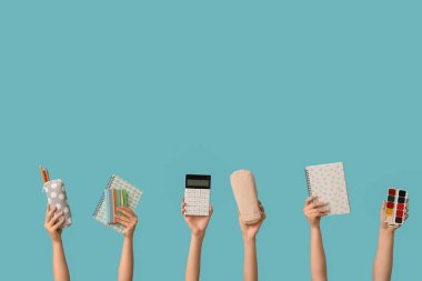 Mavi arka planda farklı okul malzemelerine sahip kadın eller.