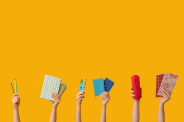Sarı arka planda farklı okul malzemelerine sahip kadın eller.
