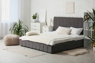 Büyük yataklı, çekmeceli ve palmiye ağaçlı şık bir yatak odası.