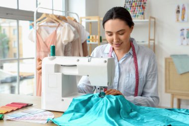 Atölyedeki masada kadın terzi dikiş dikiyor.