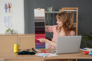 Kumaş numuneli kadın terzi atölyedeki masada görüntülü sohbet yapıyor.