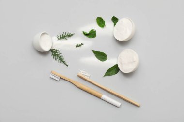 Gri arka planda yaprakları ve fırçaları olan bir kase diş tozu. Üst görünüm