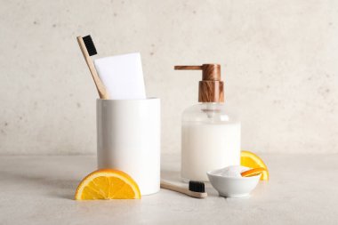 Bir kase narenciye dilimli diş tozu, tutacağı fırça ve beyaz arka planda duran sabun makinesi.