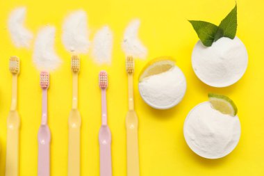 Sarı zemin üzerinde narenciye dilimleri, yapraklar ve fırçalar olan bir kase diş tozu. Üst görünüm