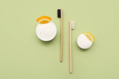 Yeşil arka planda turunçgil dilimleri ve fırçalarla dolu bir kase diş pudrası. Üst görünüm