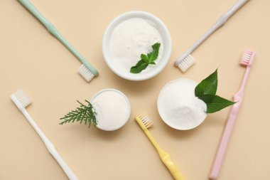 Bej arka planda yaprakları ve fırçaları olan bir kase diş tozu. Yakın çekim.