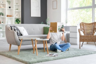 Oturma odasında iç tasarım dergisi okuyan genç bir kadın.