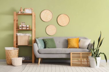 Yeşil duvarın yanında gri kanepesi ve raf ünitesi olan modern oturma odasının içinde.