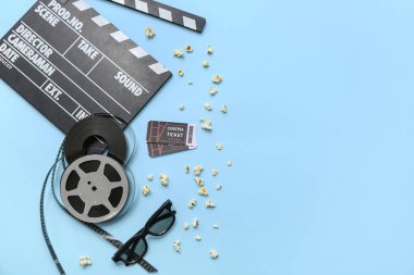 Sinema biletleri, patlamış mısır ve mavi arka planda film makaraları olan alkışlar.
