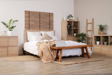 Yatak odasının içinde dizüstü bilgisayarı olan rahat bir yatak ve bank.