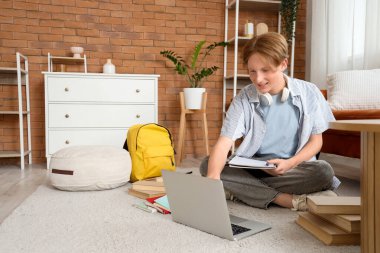 Gözlüklü, dizüstü bilgisayarlı, evde ders çalışan bir erkek öğrenci.