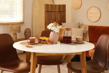 Oturma odasındaki masada sıcak çay, lezzetli haşhaşlı çörekler, çiçekler ve sonbahar yaprakları.