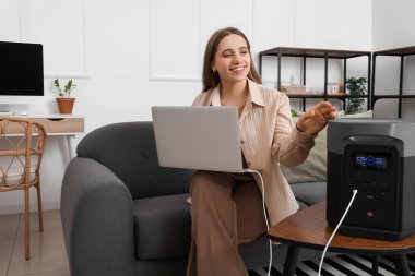 Taşınabilir elektrik santrali ve dizüstü bilgisayarı olan genç bir kadın.