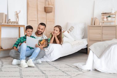 Babaları yatak odasında kitap okuyan sevimli küçük çocuklar.