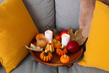 Odasındaki kanepede parlayan mumlar, elmalar ve sonbahar yapraklarıyla ahşap tepsi.