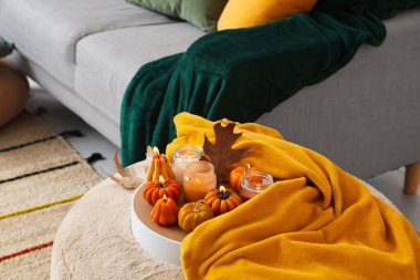 Parlayan mumlarla dolu tepsi, sonbahar yaprakları ve odada pouf üzerine ekose.