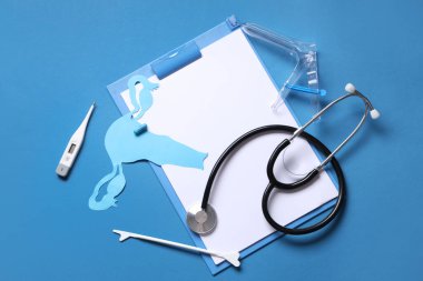 Jinekolojik malzemeler, kağıt uterus, steteskop ve mavi arka planda pano.